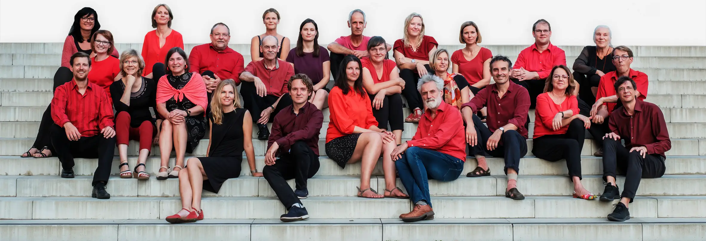 Jazzchor aus Halle sitzt gemeinsam auf Treppen, Mitglieder in roten und schwarzen Outfits