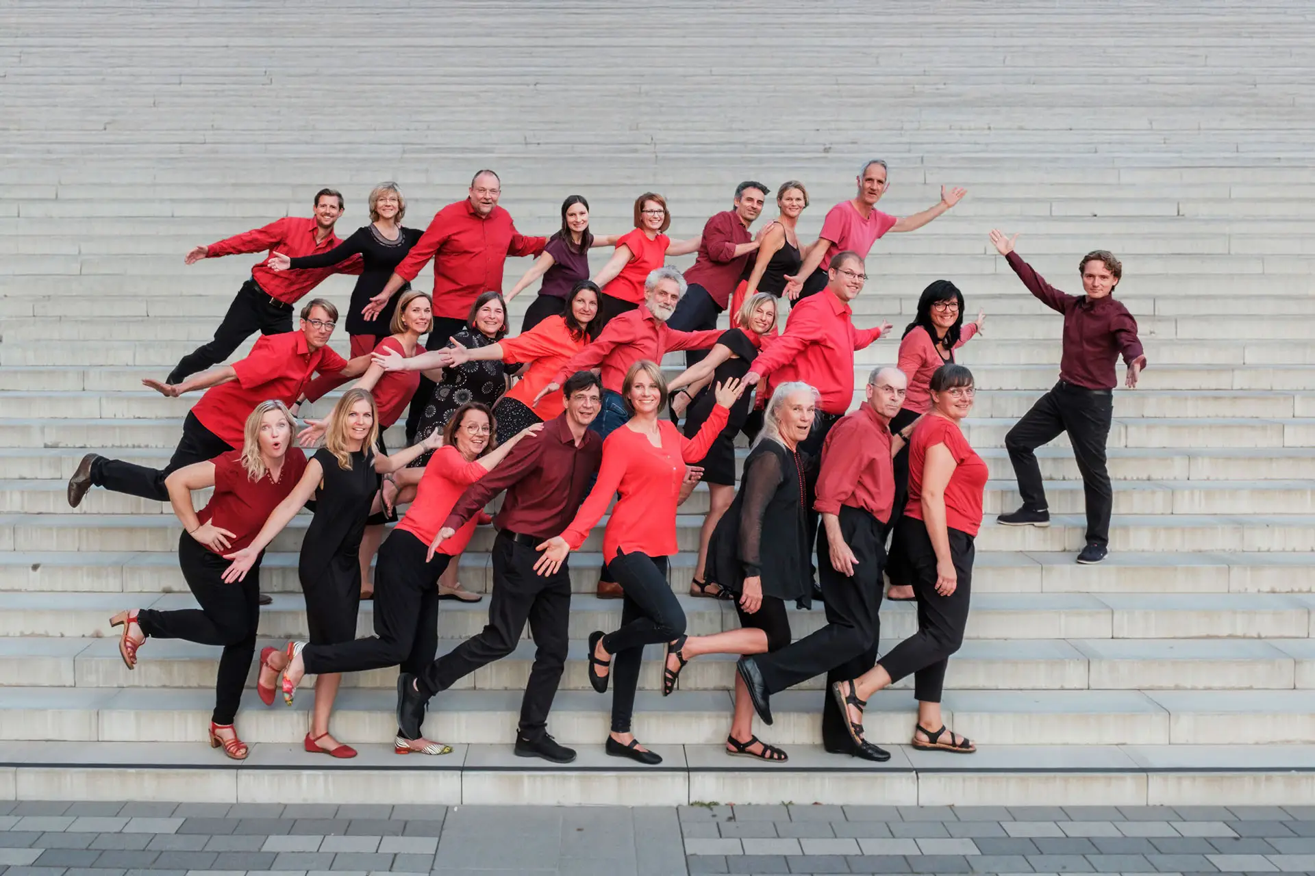 Der Jazzchor inTune posiert in dynamischen, tänzerischen Posen auf einer großen Treppe für ein fröhliches Gruppenfoto.